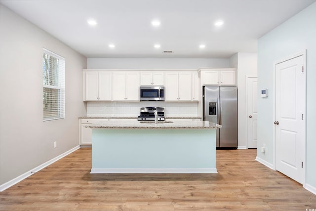 kitchen with white cabinetry, a center island with sink, light stone counters, and appliances with stainless steel finishes