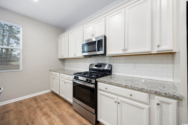 kitchen with appliances with stainless steel finishes, light wood-type flooring, tasteful backsplash, light stone counters, and white cabinetry