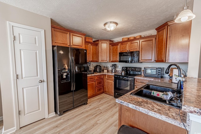 kitchen featuring black appliances, light wood-type flooring, hanging light fixtures, and a textured ceiling