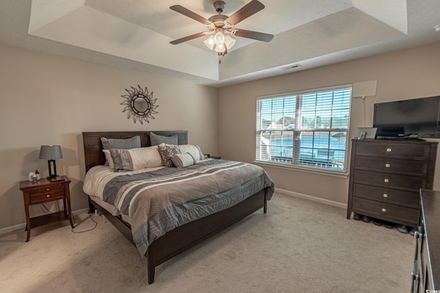 bedroom featuring ceiling fan, a raised ceiling, and light carpet