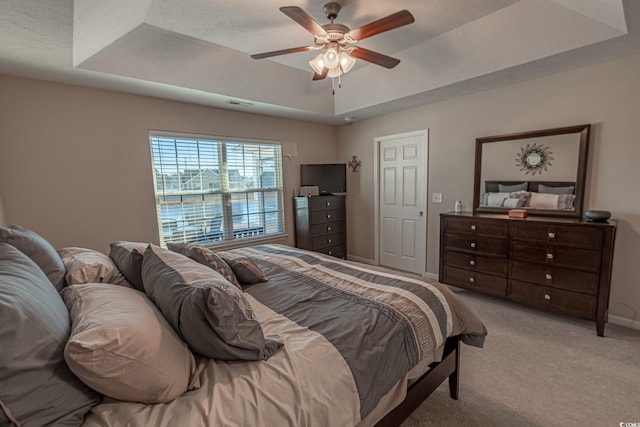 carpeted bedroom featuring a tray ceiling and ceiling fan