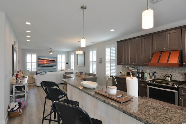 kitchen with dark brown cabinetry, stainless steel range, ventilation hood, dark stone counters, and a breakfast bar