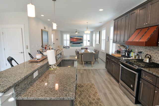 kitchen with gas range, dark brown cabinets, sink, pendant lighting, and stone countertops