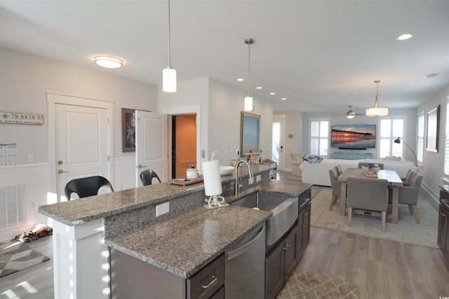 kitchen with light wood-type flooring, stainless steel dishwasher, ceiling fan, sink, and pendant lighting