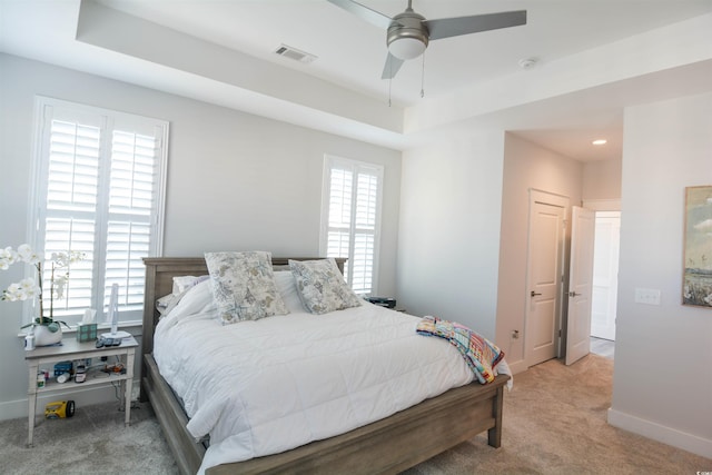 bedroom featuring ceiling fan, light carpet, and a tray ceiling