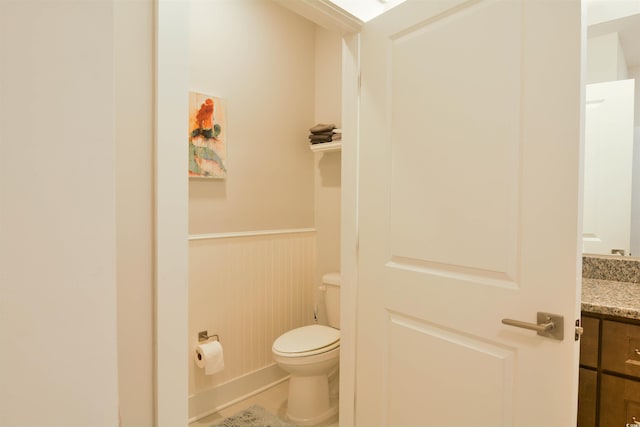 bathroom with vanity, toilet, and wood walls