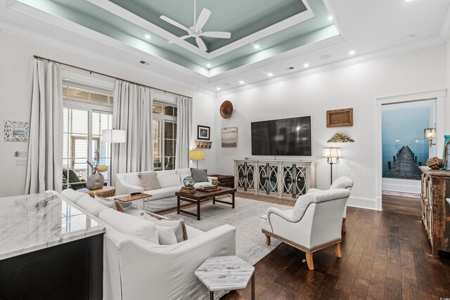 living room with ceiling fan, a tray ceiling, ornamental molding, and dark wood-type flooring