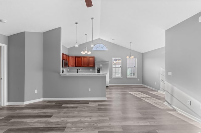 unfurnished living room featuring hardwood / wood-style floors, ceiling fan with notable chandelier, and high vaulted ceiling