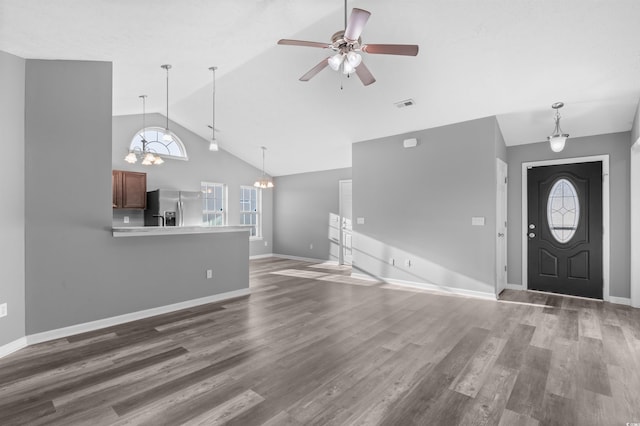 unfurnished living room with ceiling fan with notable chandelier, dark hardwood / wood-style floors, and vaulted ceiling