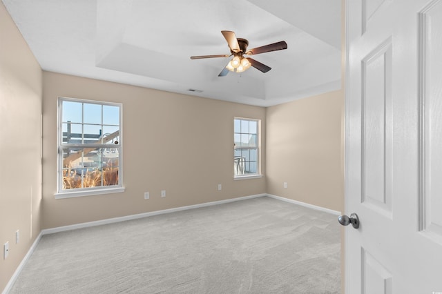 unfurnished room with ceiling fan, light colored carpet, and a tray ceiling