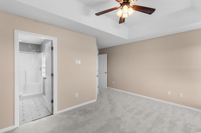 unfurnished bedroom featuring a tray ceiling, ensuite bath, ceiling fan, and light carpet