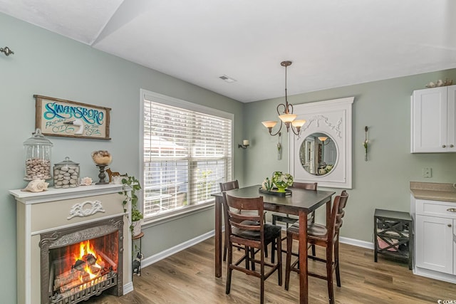 dining area featuring a warm lit fireplace, visible vents, baseboards, and wood finished floors