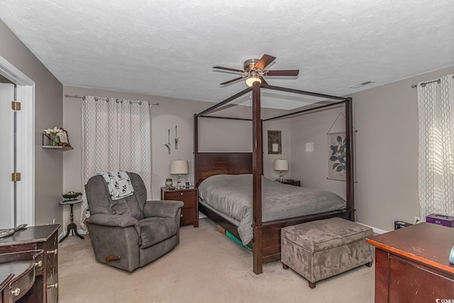 bedroom featuring a ceiling fan, light colored carpet, visible vents, and a textured ceiling