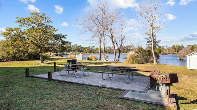 view of home's community with a lawn, a patio area, a water view, and a storage shed