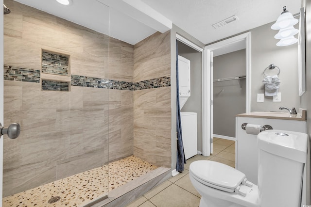 bathroom with tile patterned floors, sink, toilet, stacked washer / drying machine, and a tile shower