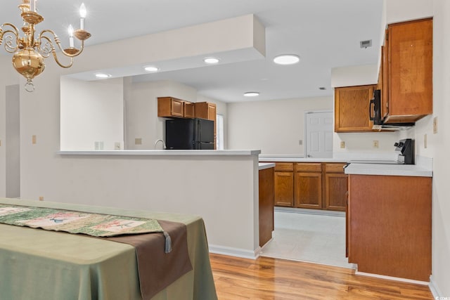 kitchen featuring sink, an inviting chandelier, hanging light fixtures, black appliances, and light wood-type flooring