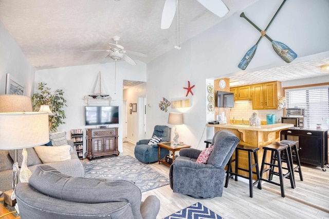 living area with ceiling fan, high vaulted ceiling, and light wood finished floors