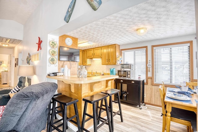 kitchen with kitchen peninsula, backsplash, a breakfast bar, a textured ceiling, and light hardwood / wood-style flooring