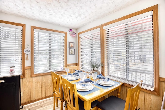 dining space with a textured ceiling, wood walls, wainscoting, and light wood-style floors