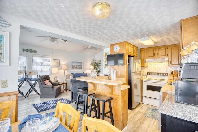 kitchen with white range with electric stovetop, range hood, light countertops, a ceiling fan, and freestanding refrigerator