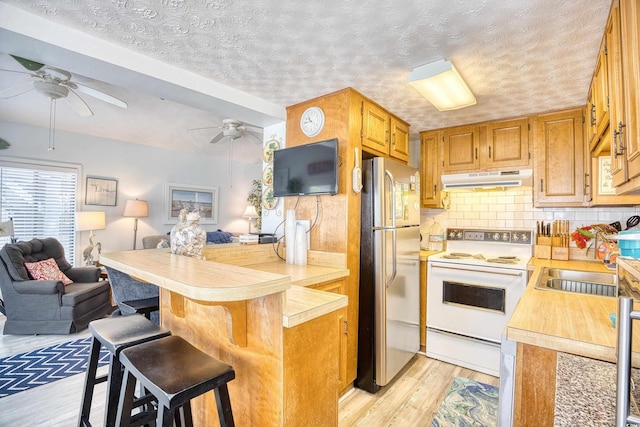 kitchen with white electric stove, stainless steel fridge, a textured ceiling, a breakfast bar area, and decorative backsplash