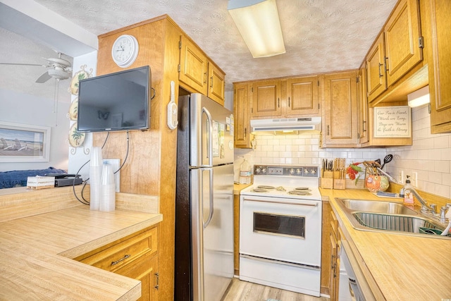 kitchen featuring white appliances, a sink, a textured ceiling, under cabinet range hood, and backsplash