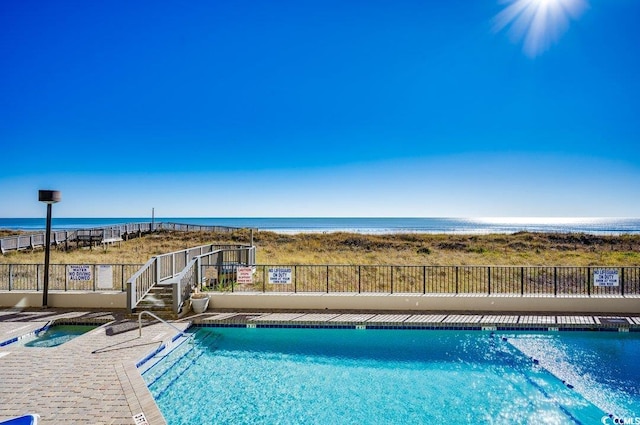 pool featuring a community hot tub, a patio area, a water view, and fence