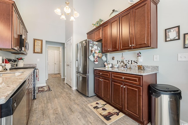 kitchen featuring light wood-type flooring, stainless steel appliances, light stone counters, and a notable chandelier