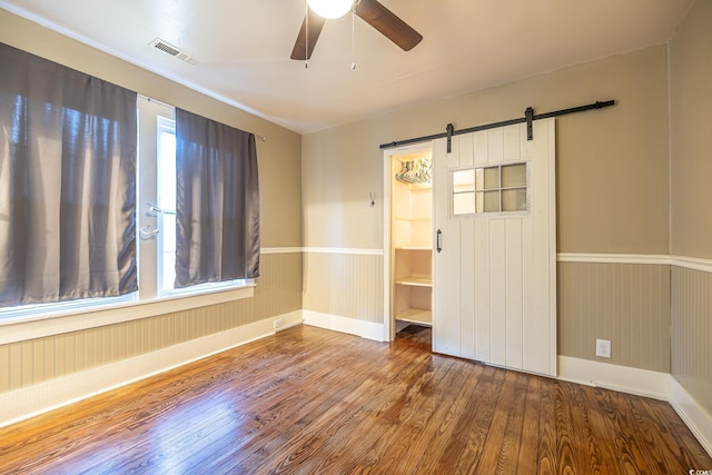 empty room featuring ceiling fan, hardwood / wood-style flooring, and a barn door