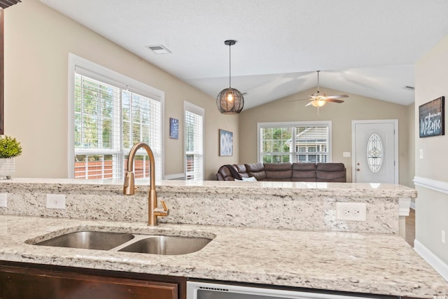 kitchen with vaulted ceiling, pendant lighting, sink, ceiling fan, and light stone counters