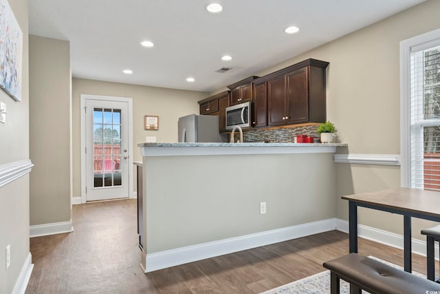 kitchen with a wealth of natural light, dark brown cabinets, decorative backsplash, and appliances with stainless steel finishes