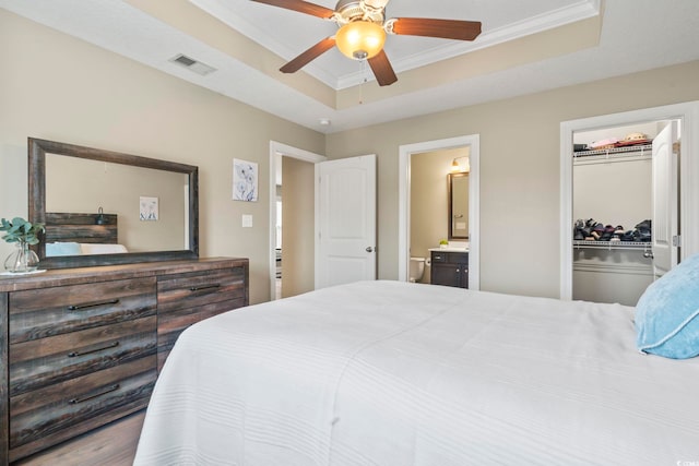 bedroom featuring crown molding, ensuite bath, a tray ceiling, and a spacious closet