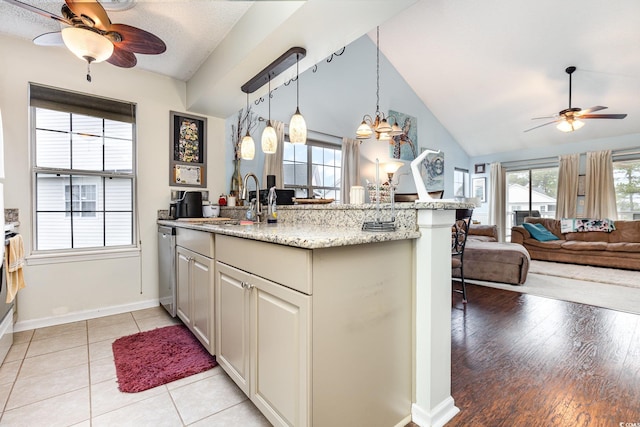 kitchen featuring pendant lighting, dishwasher, ceiling fan, vaulted ceiling, and light stone countertops