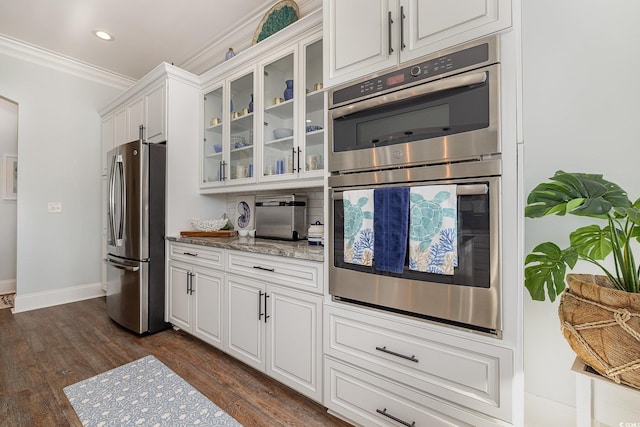 kitchen featuring white cabinets, dark hardwood / wood-style floors, ornamental molding, appliances with stainless steel finishes, and light stone counters