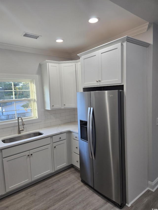 kitchen featuring sink, white cabinetry, backsplash, stainless steel refrigerator with ice dispenser, and light wood-type flooring