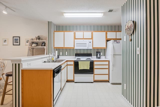 kitchen with a breakfast bar, white appliances, sink, a textured ceiling, and white cabinetry