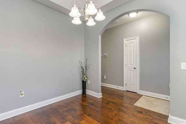 spare room with dark hardwood / wood-style flooring and an inviting chandelier