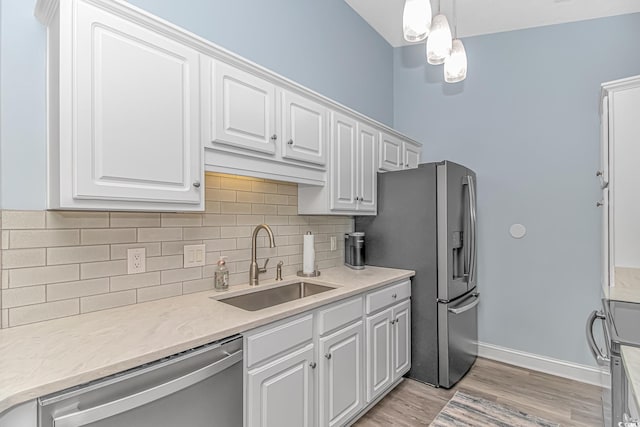 kitchen with appliances with stainless steel finishes, sink, white cabinets, and decorative light fixtures