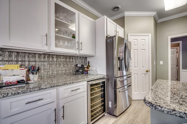 kitchen with light stone countertops, beverage cooler, stainless steel fridge, white cabinets, and ornamental molding