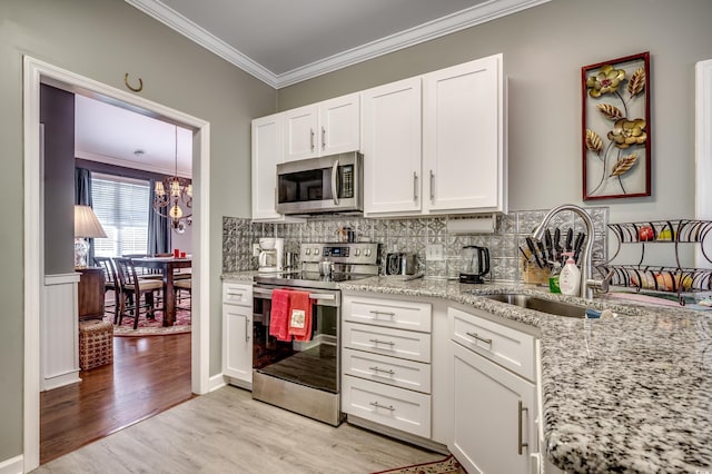 kitchen with light stone counters, light hardwood / wood-style floors, stainless steel appliances, white cabinets, and ornamental molding