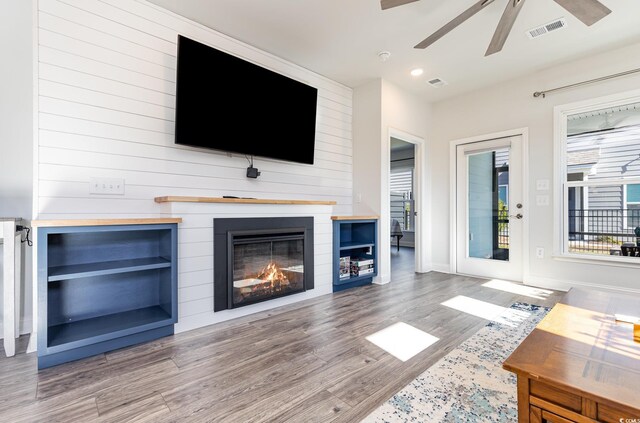 living room featuring built in shelves, a large fireplace, and wood-type flooring