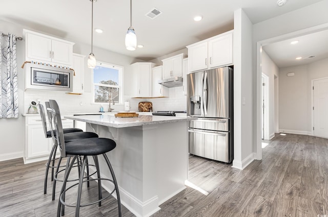 kitchen featuring a kitchen island, light hardwood / wood-style flooring, decorative light fixtures, white cabinets, and appliances with stainless steel finishes