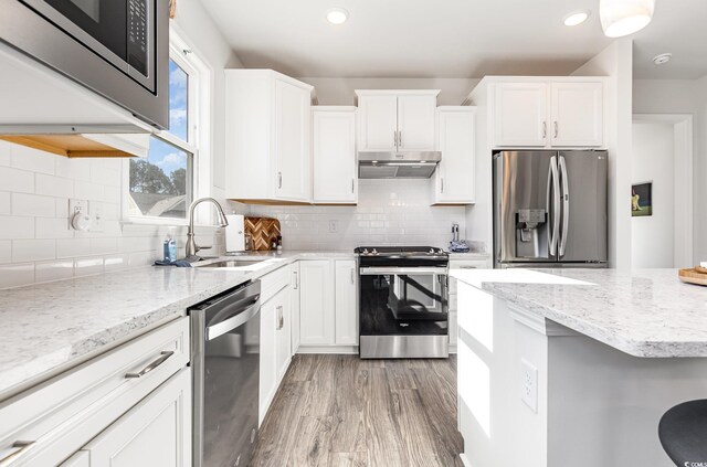 kitchen with appliances with stainless steel finishes, backsplash, sink, light hardwood / wood-style floors, and white cabinetry