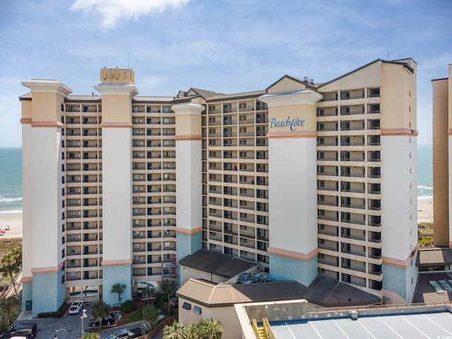 view of building exterior with a water view, uncovered parking, and a view of the beach