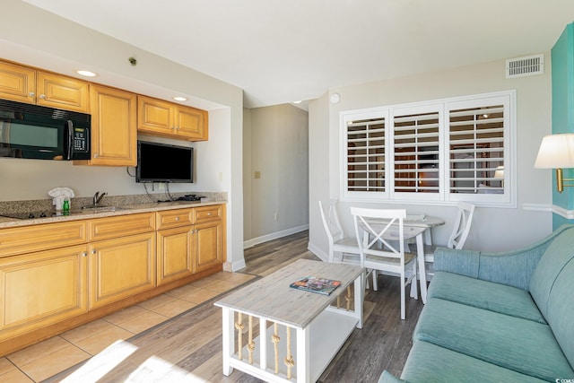 kitchen featuring visible vents, baseboards, black microwave, light wood-type flooring, and light stone counters