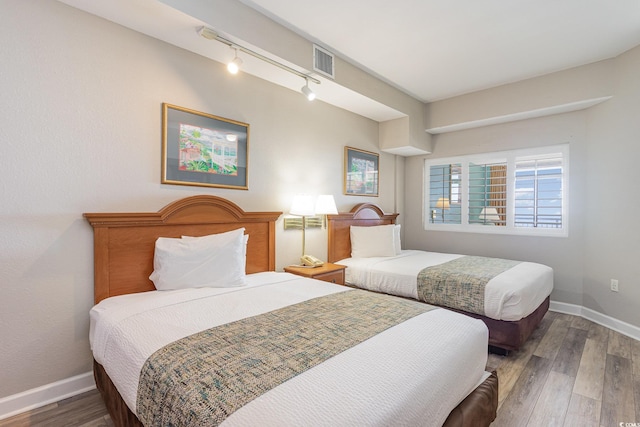 bedroom featuring track lighting, wood finished floors, visible vents, and baseboards