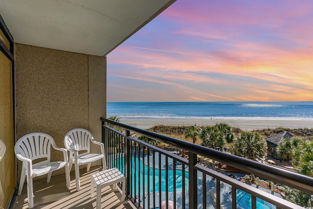 balcony at dusk featuring a beach view and a water view