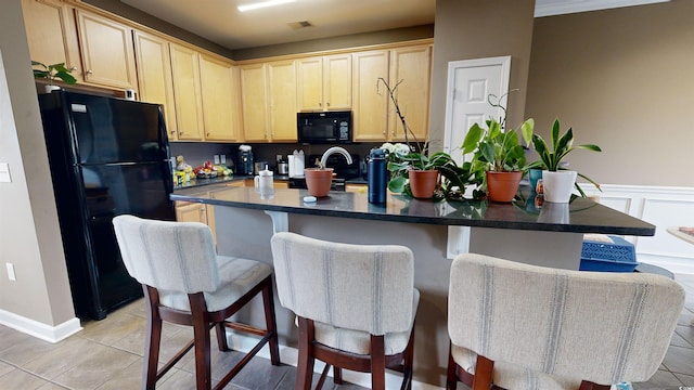 kitchen with a kitchen breakfast bar, an island with sink, light brown cabinetry, light tile patterned floors, and black appliances