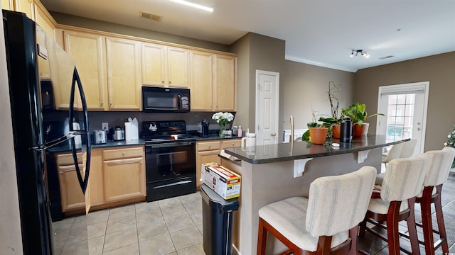 kitchen with light brown cabinets, black appliances, a center island with sink, light tile patterned flooring, and a breakfast bar area