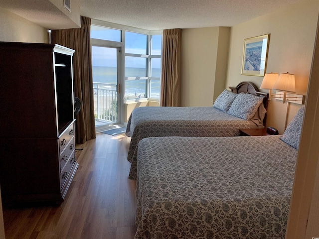 bedroom with floor to ceiling windows, a water view, a textured ceiling, wood finished floors, and access to outside